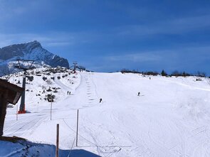Snow-covered slope with skiers and a chairlift.