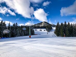 Eine schneebedeckte Piste mit Sesselliften und blauen Himmel.