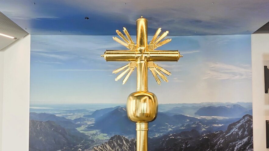 Ein goldenes Kreuz vor einer beeindruckenden Berglandschaft.