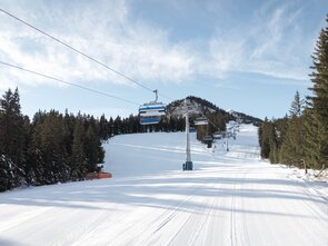 Schneebedeckte Piste mit Skilifte und Bäumen im Hintergrund.