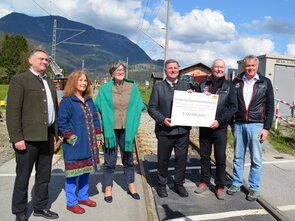 Six people are standing on a railroad crossing, two of them holding a check for €2.3 million to fund railway infrastructure. 