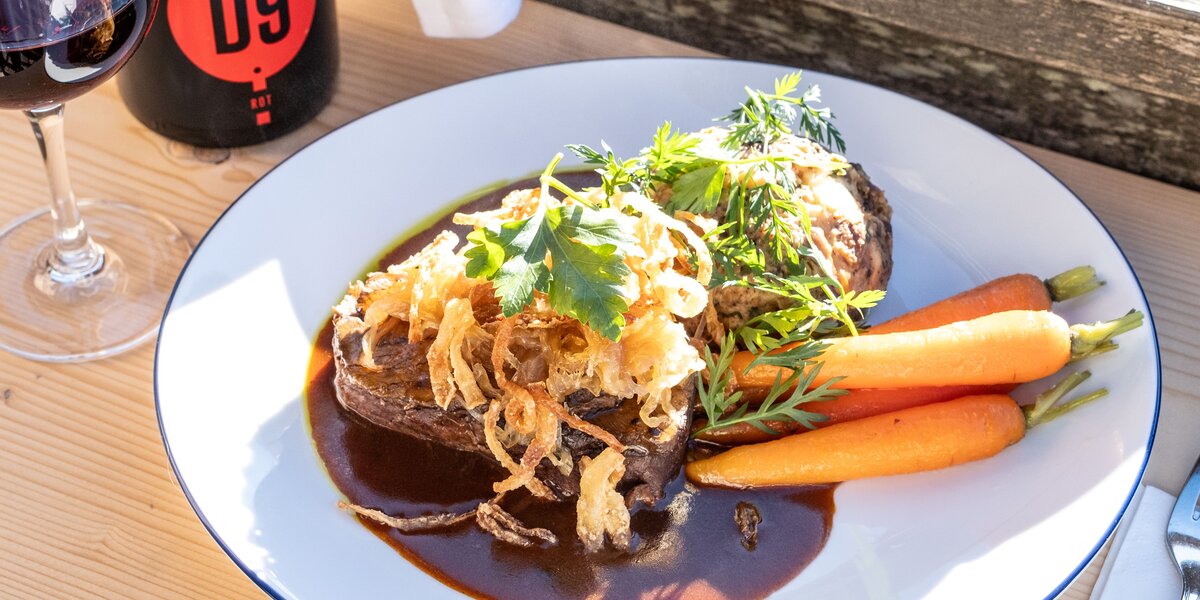 Zartes Rindfleischgericht mit karamellisierten Zwiebeln, Karotten und einem Glas Rotwein.