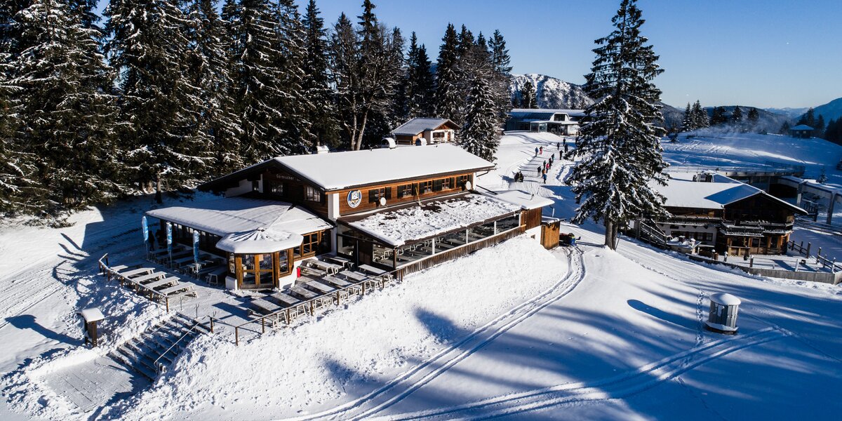 Schneebedeckte Berghütte umgeben von Bäumen und Skipisten.