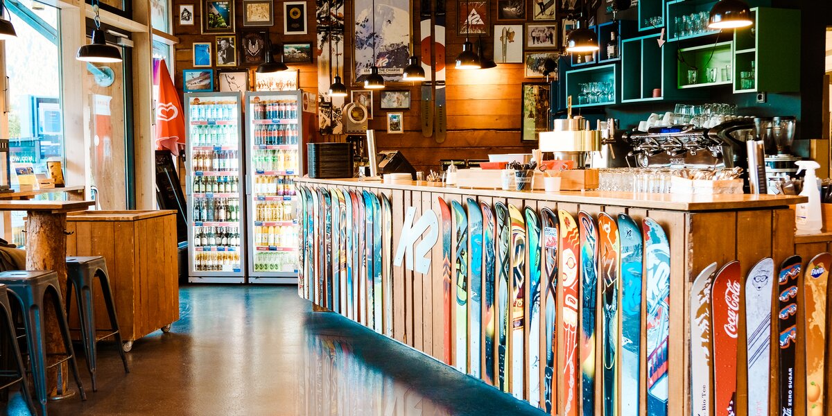 Innensicht einer Bar mit Skiern als Theke und farbenfrohen Bildern an der Wand.