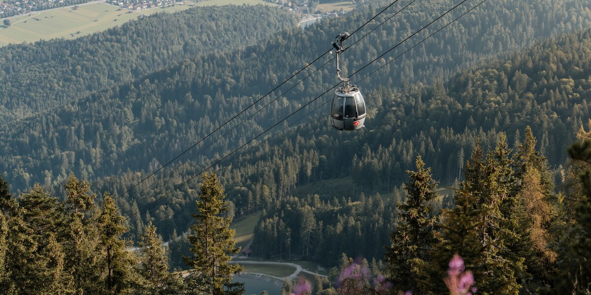 Eine Seilbahn fährt über dichte Wälder in den Bergen über Garmisch-Partenkirchen.