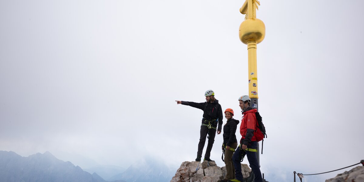 Three climbers at a mountain summit featuring a golden cross.