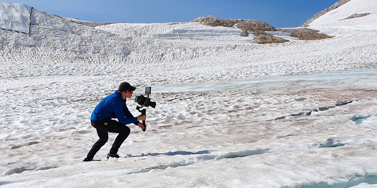 A man with a camera stands on the snow-covered glacier and films. 