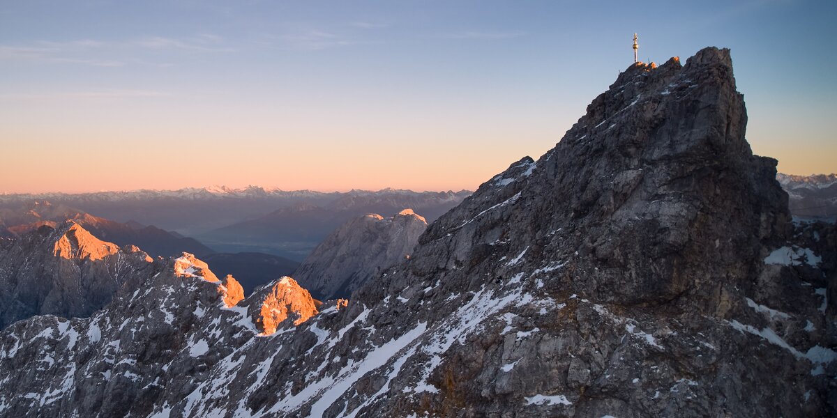 Atemberaubender Blick auf angezuckerte Berge und das Gipfelkreuz der Zugspitze bei Sonnenuntergang.