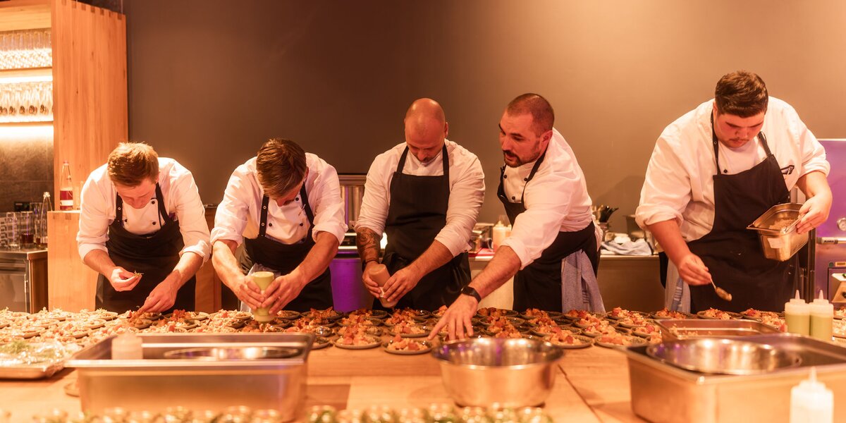 Several chefs prepare a dish for a menu on numerous plates in a row. 