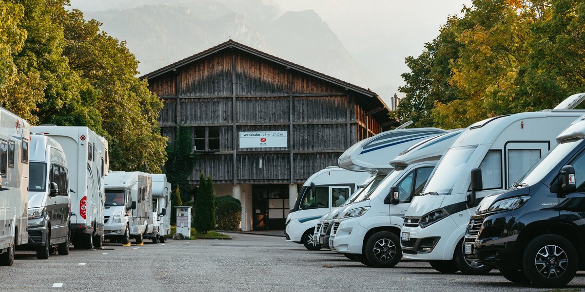Eine Reihe von Wohnmobilen vor einem Holzgebäude mit Bergen im Hintergrund.