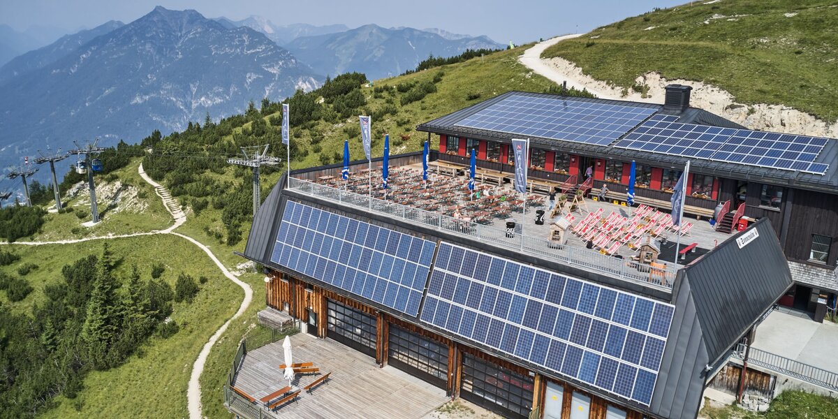 Luftaufnahme eines Bergrestaurants mit Solarpanelen und gemütlicher Außenterrasse.