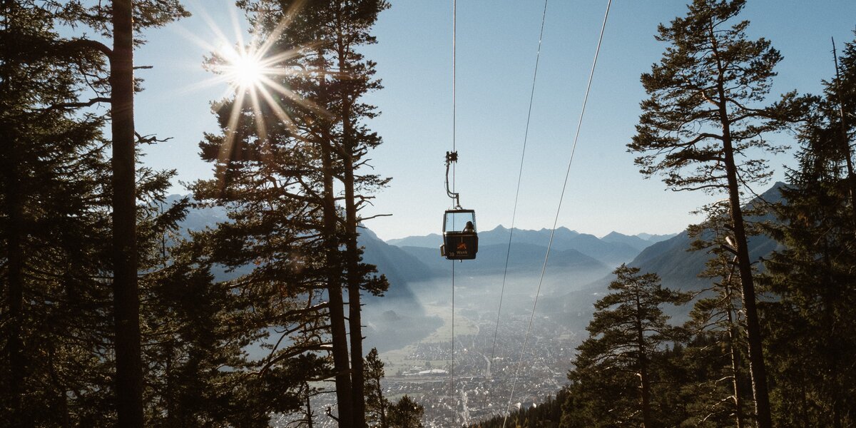 Eine Seilbahn fährt über einen Wald mit Blick auf die Stadt im Tal.