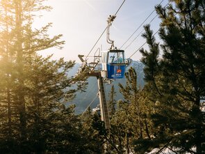 Eine Seilbahn mit Blick auf Berge und Bäume im Sonnenlicht.