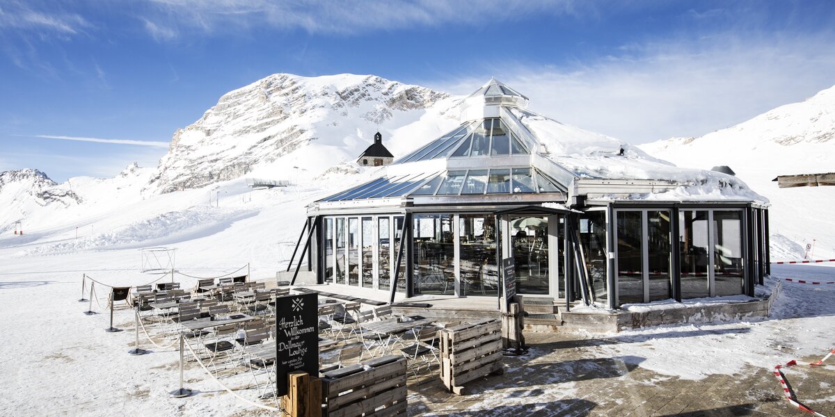 Ein gläsernes Restaurant in schneebedeckter Berglandschaft.