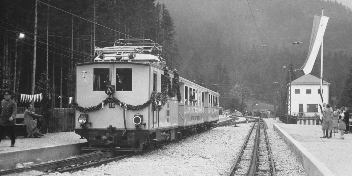 Ein historischer Triebwagen steht am Bahnhof umgeben von Bäumen.