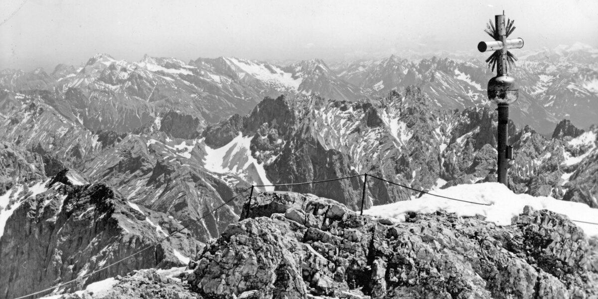 Panoramic view of the Alps with summit cross and snow.