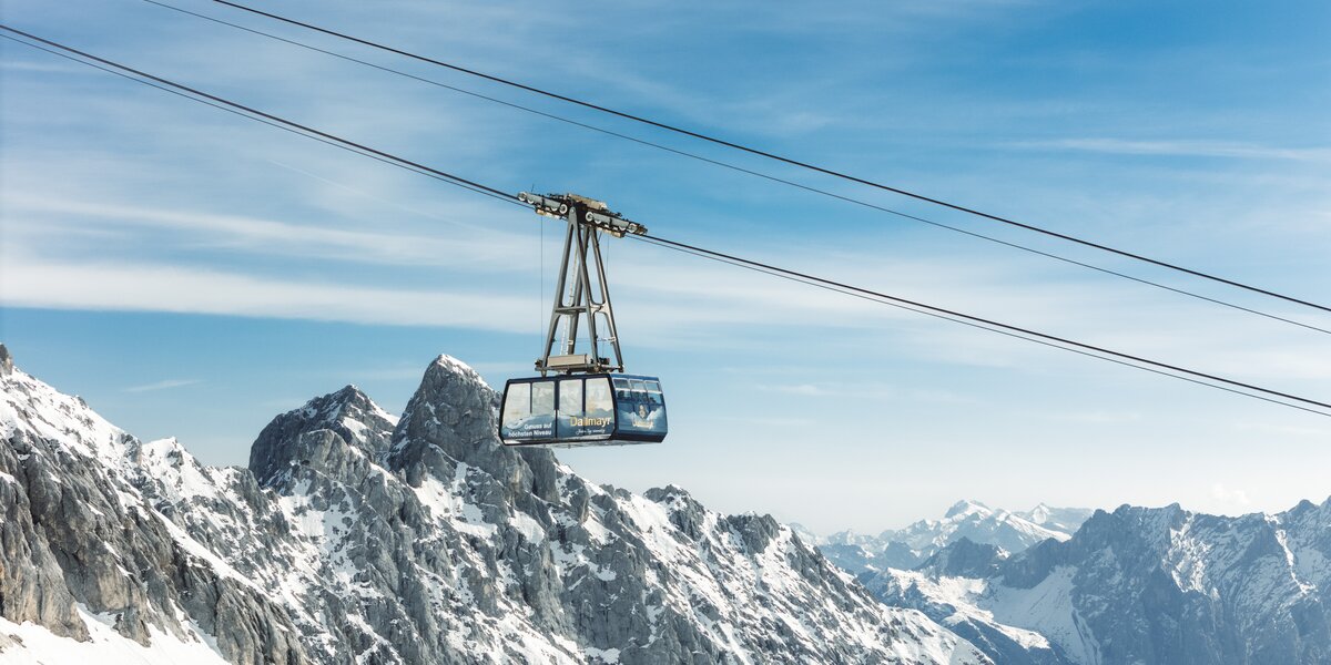 A cable car glides over majestic snow-covered mountain peaks.