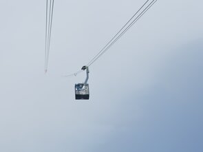 Eine Seilbahn-Kabine fährt in ein Wolkenmeer. 