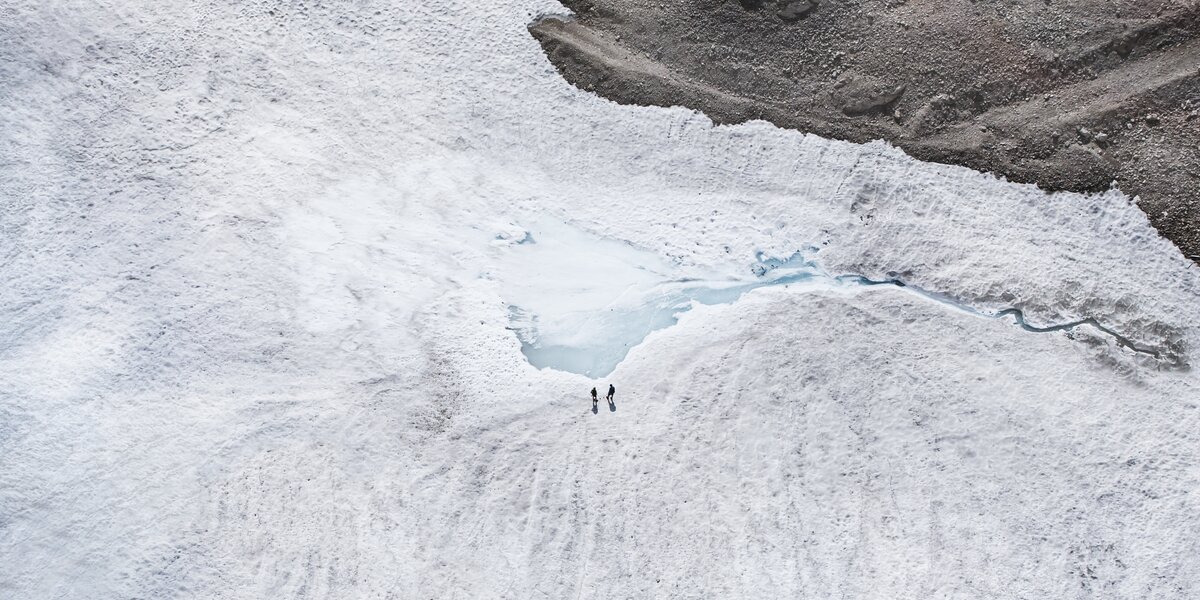 Two people stand on a glacier with water pools.