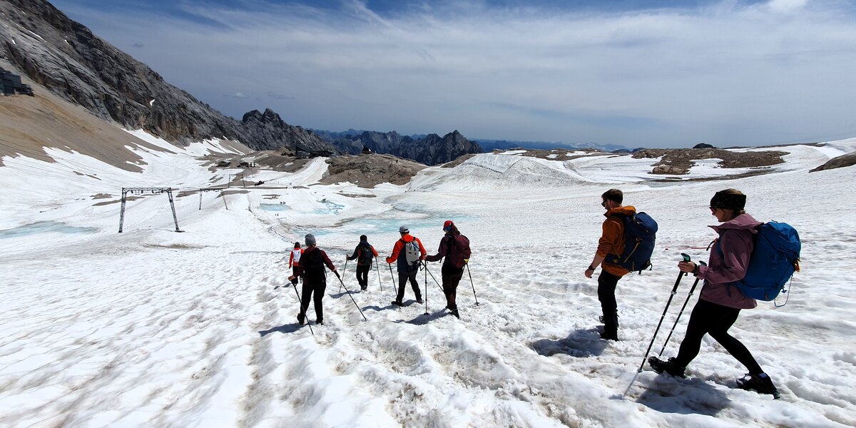 Several people with backpacks and hiking poles walk across the glacier in summer.
