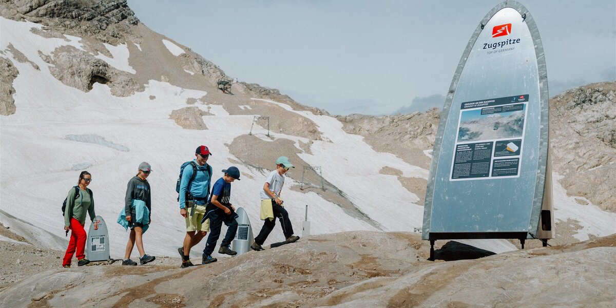 A family hikes on the Zugspitze between two information stations on the glacier trail with the Nördliche Schneeferner glacier in the background.