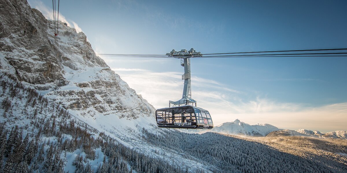 Eine Seilbahn schwebt über verschneite Berge und Wälder.