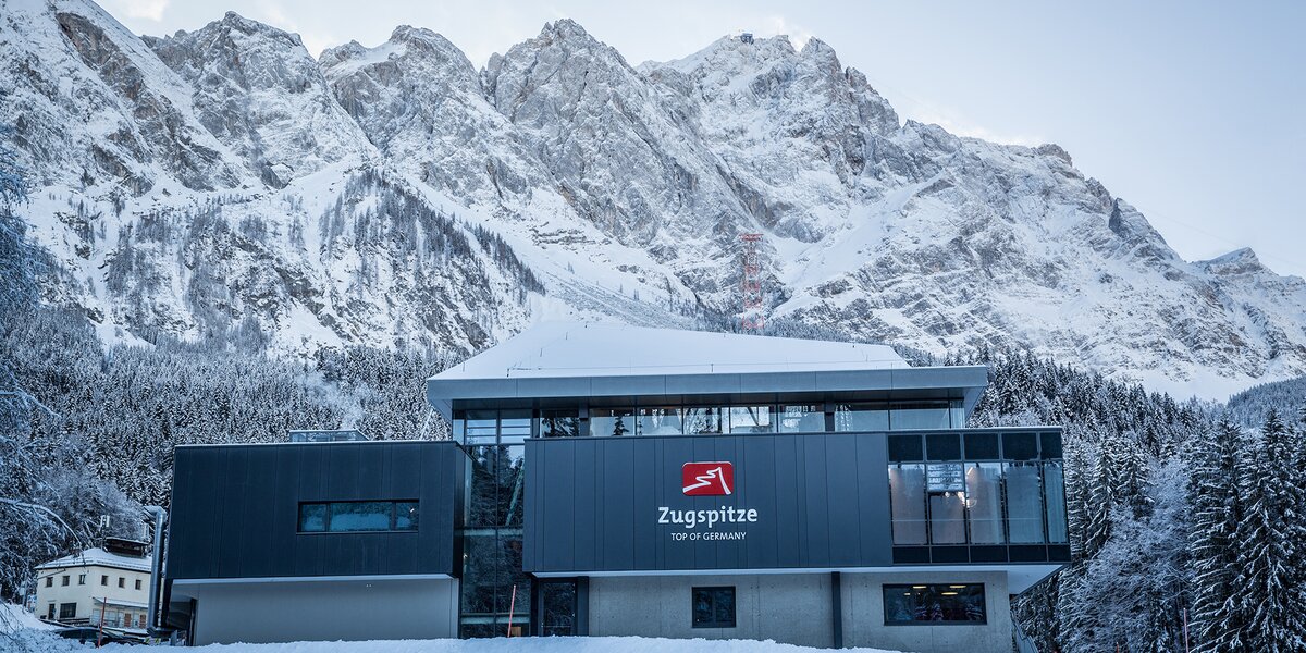 Die Talstation der Seilbahn Zugspitze in winterlicher Umgebung, umgeben von Berggipfeln.