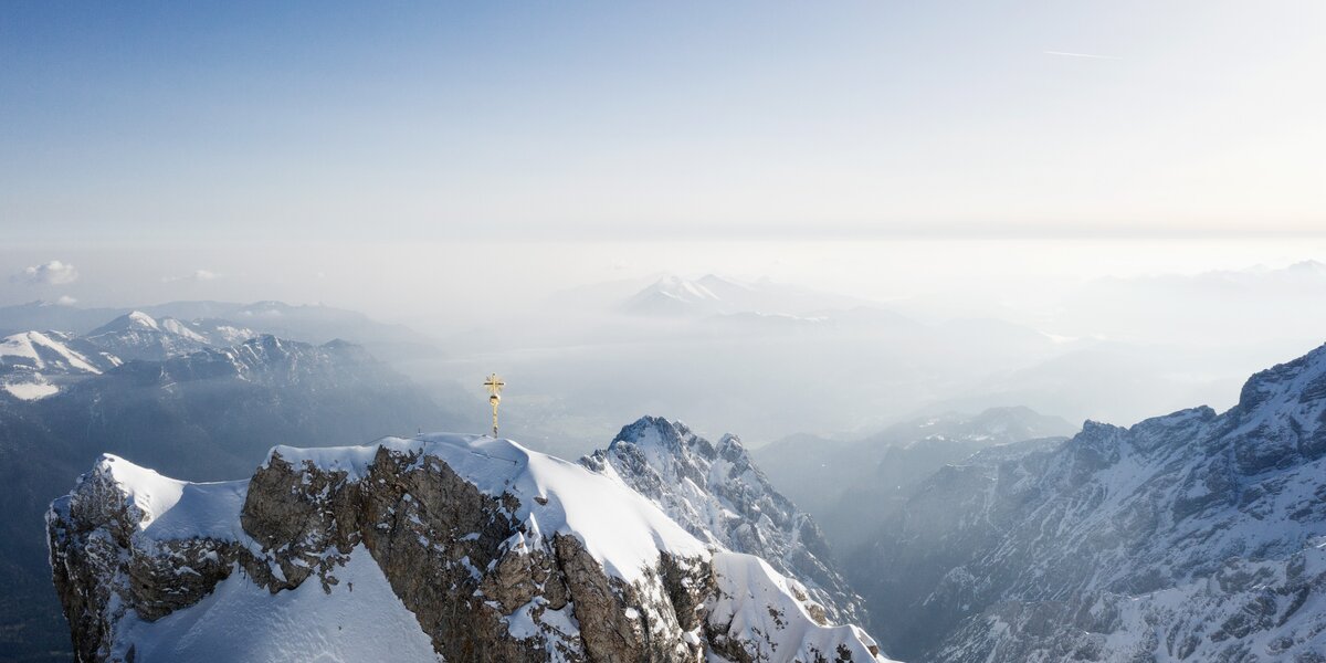 Schneebedeckter Berggipfel mit goldenen Kreuz in der Ferne.