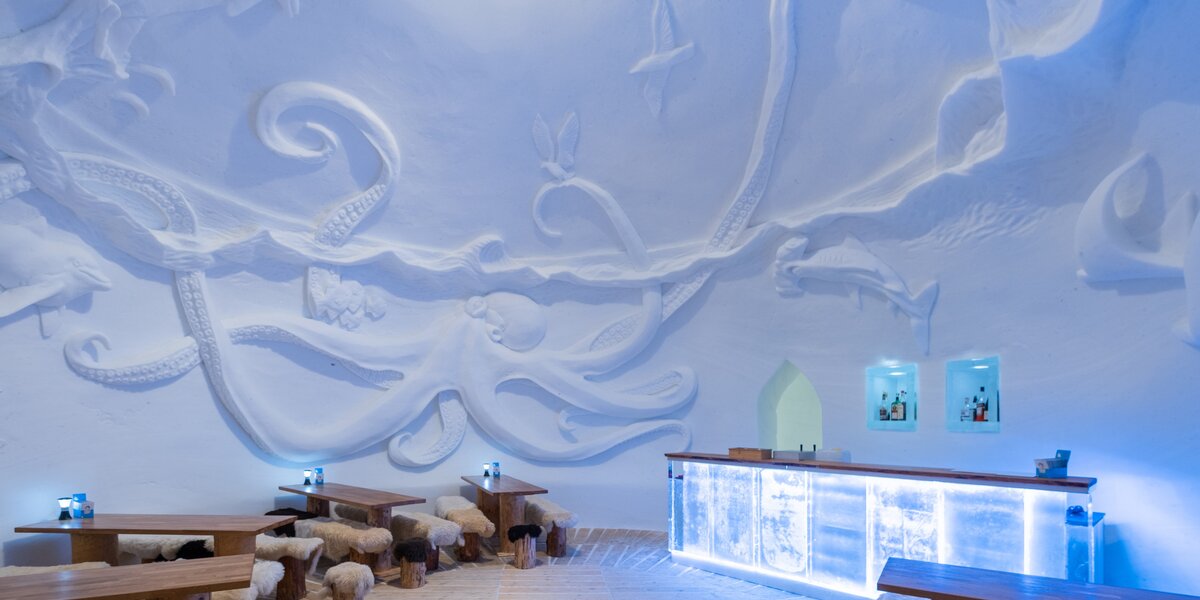 Aesthetic ice room with curved snow sculptures and wooden bar.