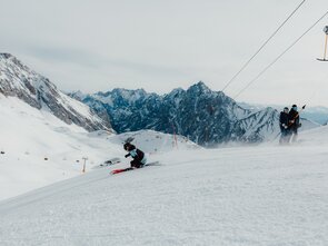 Ein Skifahrer fährt im Skigebiet Zugspitze mit schöner Aussicht auf die Berge, hinter ihm stehen zwei Personen im Schlepplift. 